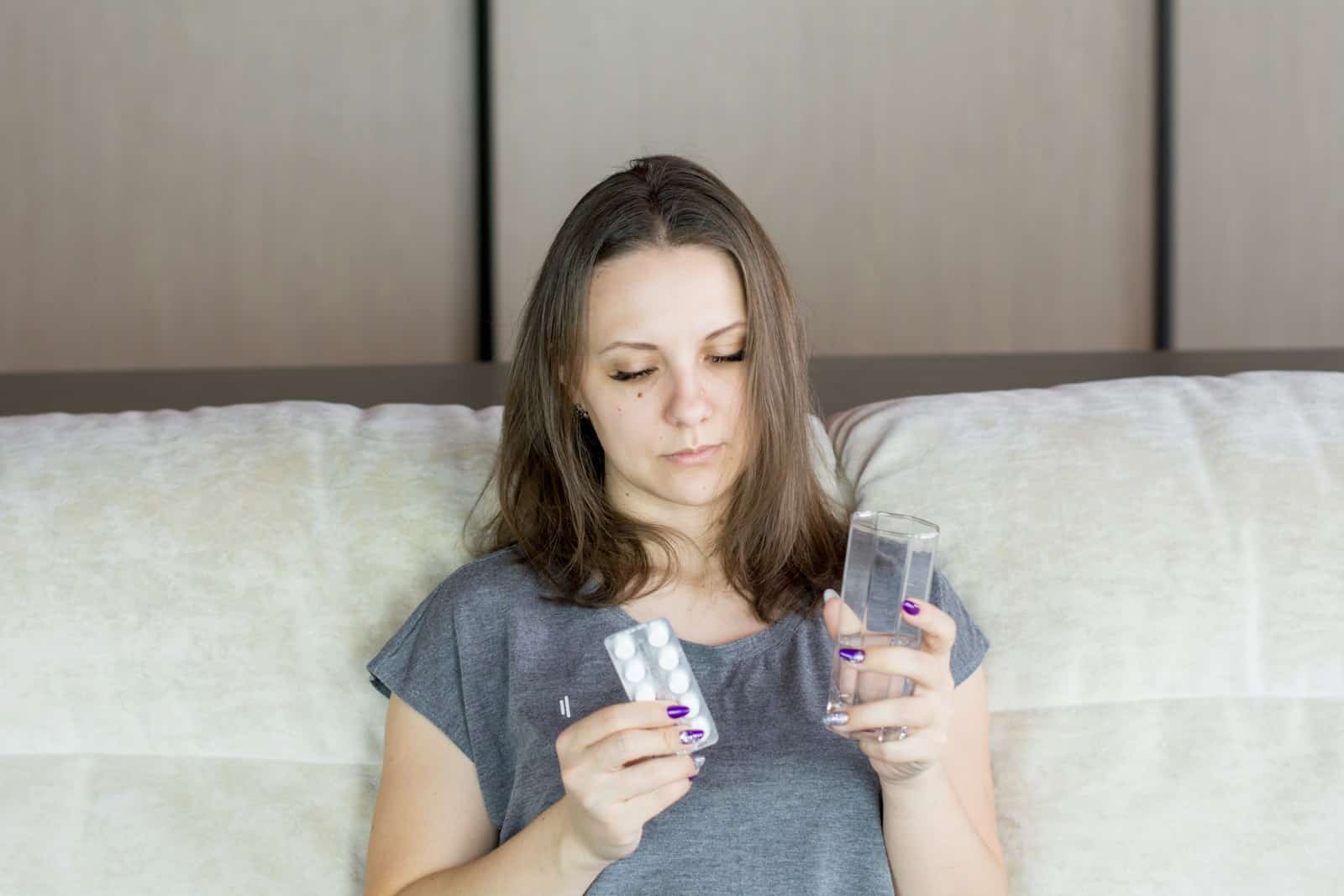 An unwell woman sitting on a couch looking at her medications