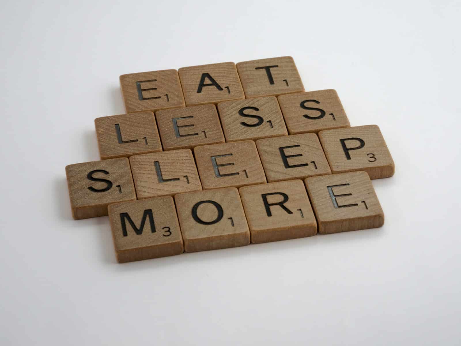 brown wooden blocks on white surface. Eat Less Sleep More