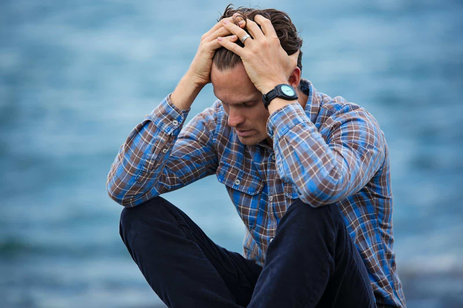 Man in Blue and Brown Plaid Shirt with head in hands. Hypnosis for Anxiety